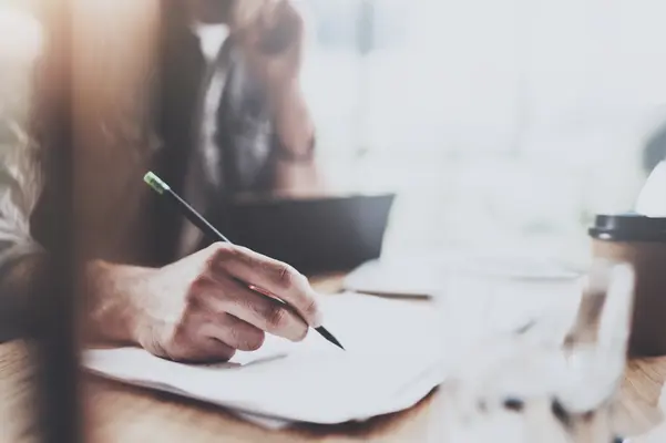 Eine unscharfe Silhouette im Anzug läuft von links nach rechts. Dahinter sitzt ein Mann auf einem Sofa.
